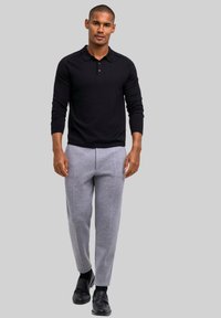 Czarna koszulka polo z długim rękawem i kołnierzykiem, zestawiona z jasnoszarymi zwężanymi spodniami dresowymi i czarnymi butami. Prosty, nowoczesny design.