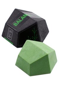 Stały szampon w geometrycznym zielonym kształcie, z textured powierzchnią, umieszczony w czarnym opakowaniu z zielonym tekstem i motywami liści.