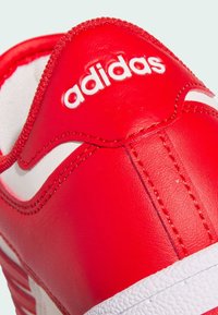 Crvene kožne tenisice s bijelim detaljima, teksturiranom gumenom potplatom i istaknutim bijelim "adidas" logotipom prošivenim na jeziku.