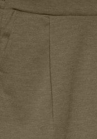 Nærbillede af brune stofbukser, der viser forreste folder og detaljer ved sidelommen.