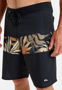 Bañador negro con un patrón de hojas tropicales multicolores en la parte inferior. Cuenta con una cintura con cordón y tejido texturizado.
