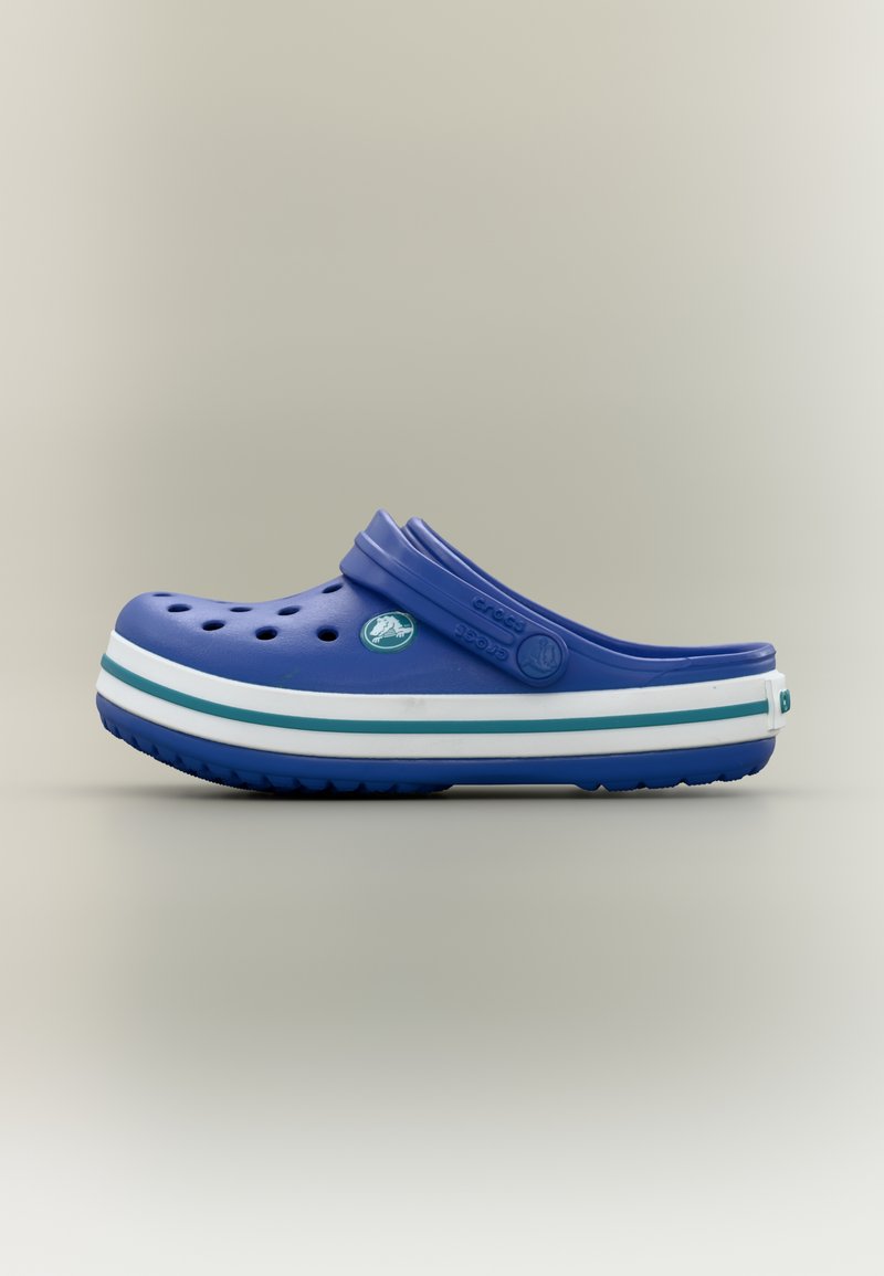 Μπλε clog Crocs με οπές αερισμού, λευκή και πετρόλ ριγωτή σόλα, ρυθμιζόμενο λουράκι στην φτέρνα, σε απλό ανοιχτό γκρι φόντο.
