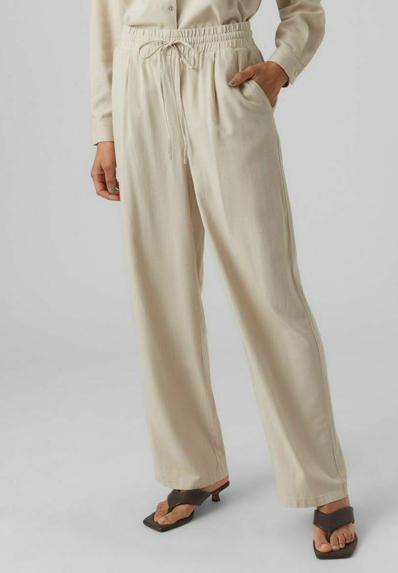 Pantalons larges beige clair avec une taille élastique et un cordon de serrage, dotés de poches latérales et d'un tissu lisse légèrement texturé.
