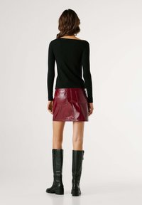 Μαύρο ριμπ πουκάμισο με μακριά μανίκια συνδυασμένο με γυαλιστερή μπορντό μίνι φούστα. Το μοντέλο φοράει μαύρες μπότες με τακούνι μέχρι το γόνατο. Πλάγια όψη, χωρίς ορατά μοτίβα.