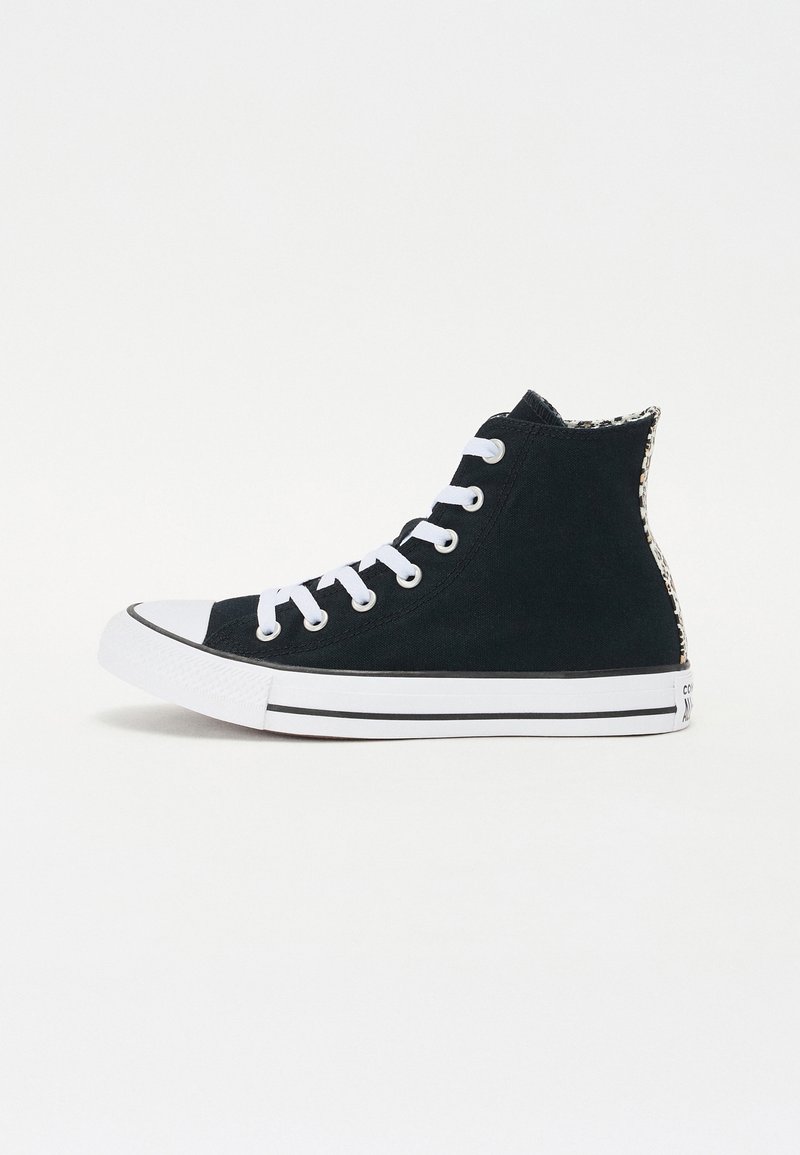Sorte høyhælte sneakers laget av lerret, med hvite snører, en gummitåhette og en teksturert aksent ved hælen. Svarte og hvite stripete såler.