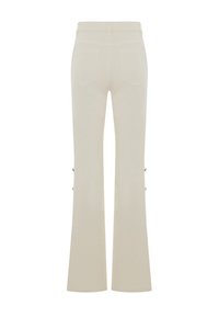 Pantaloni beige a zampa d'elefante realizzati in tessuto morbido. Presentano una vita media, tasche posteriori e dettagli con bottoni laterali. Design semplice, senza motivi.