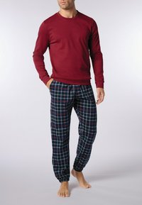 Maglia rossa a maniche lunghe abbinata a pantaloni da pigiama a quadri blu navy con motivi bianchi, blu e rossi, polsini elastici e tessuto testurizzato.