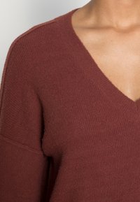 Sweater de decote em V em tecido de malha vermelho-escuro; apresenta uma superfície texturizada, mangas largas e um corte descontraído.