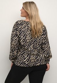 Blusa a maniche lunghe con stampa animale nera e beige. Tessuto morbido e testurizzato con una vestibilità rilassata e orlo curvo.