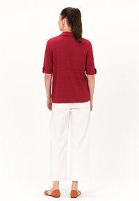 Top corto rojo de manga corta con cuello y mangas enrolladas, combinado con pantalones anchos blancos y zapatos planos marrones. Diseño simple y texturizado.