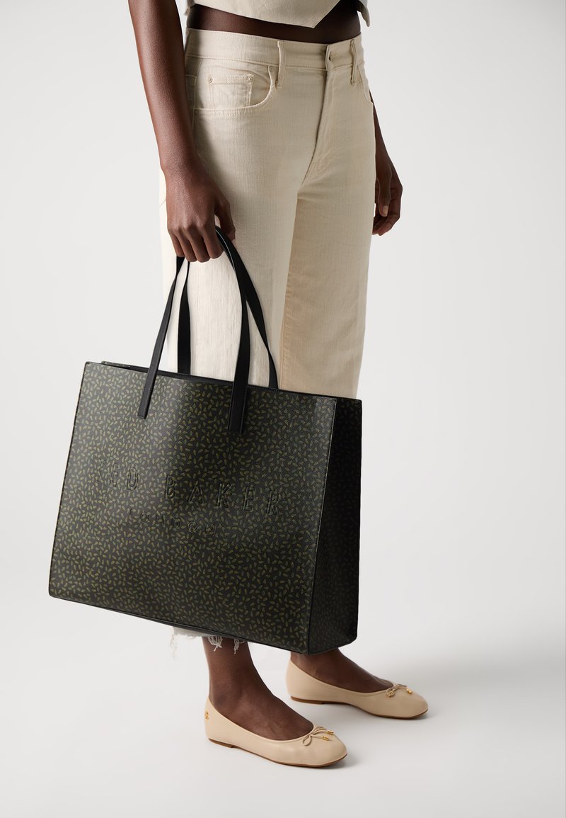 Zwarte en groene gestreepte tote bag met twee lange hengsels, voorzien van reliëf branding. Het materiaal lijkt glanzend met textuurdetails.