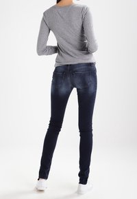 Tmavě modré úzké džíny s vybledlým efektem, zadními kapsami a vysokým pasem, v kombinaci s přiléhavým šedým tričkem s dlouhým rukávem. Bílé tenisky.