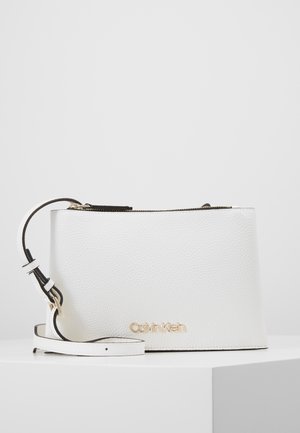 Witte getextureerde leren polstasje met gouden Calvin Klein-logo en verstelbare band, geplaatst op een witte ondergrond.