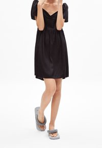 Černé krátké šaty s nabíranými rukávy, hladkou texturou a výstřihem do V. Šedé žabky s širokými pásky. Jednoduchý, minimalistický design.