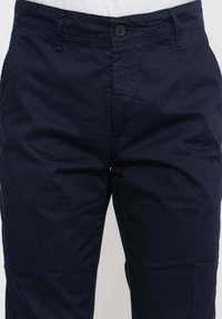Chino in cotone blu navy con taglio dritto, dotato di chiusura a bottone e due tasche anteriori. Il tessuto presenta una texture liscia.