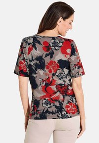 Blusenshirt mit kurzen Ärmeln und floralem Muster auf grauem Hintergrund, das große rote, schwarze und cremefarbene Blumen zeigt, mit U-Boot-Ausschnitt und taillierter Silhouette.