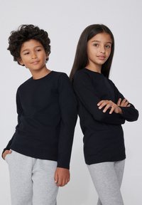 Dvě děti v černých tričkách s dlouhým rukávem. Chlapec má kudrnaté vlasy a dívka má rovné vlasy. Obě děti mají na sobě šedé tepláky.