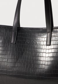 Czarna torba typu tote z fakturą krokodyla i wytłoczonym logo "Stylein", z dwiema szytymi skórzanymi uchwytami.