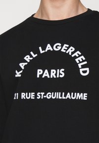 Maglietta nera con testo bianco "KARL LAGERFELD PARIS 21 RUE ST-GUILLAUME" centrato sul petto.