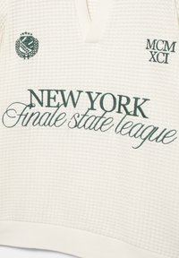 Bílá texturovaná látka se zeleným vyšívaným textem "NEW YORK finale state league" a "MCM XCI" a malým emblémem s hvězdami a listy.