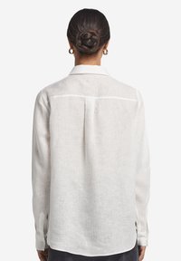 Camicia bianca in lino con taglio dritto, maniche lunghe e piega sul retro. Polsini con bottoni e design del colletto classico.