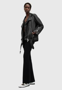Black leather biker jacket with studded shoulder accents, zippered pockets, paired with flared black pants and silver shoes.