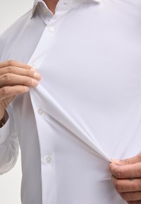 Weißes Hemd mit Knöpfen aus glattem Stoff, mit einem spitzen Kragen, sichtbaren Knöpfen und einer Nahaufnahme der Stofftextur.