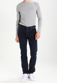 Grå randig långärmad skjorta i klassisk passform, kombinerad med mörkblå jeans och vita sportskor med snörning.