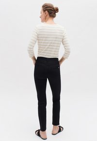 Maglietta a righe beige e crema con maniche lunghe, jeans neri aderenti, indossati con sandali neri. Inquadratura sul profilo posteriore dell'outfit casual.