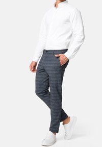 Biała koszula z długim rękawem w połączeniu z granatowymi spodniami w kratę. Spodnie mają wzór w kratę i są zestawione z białymi tenisówkami.