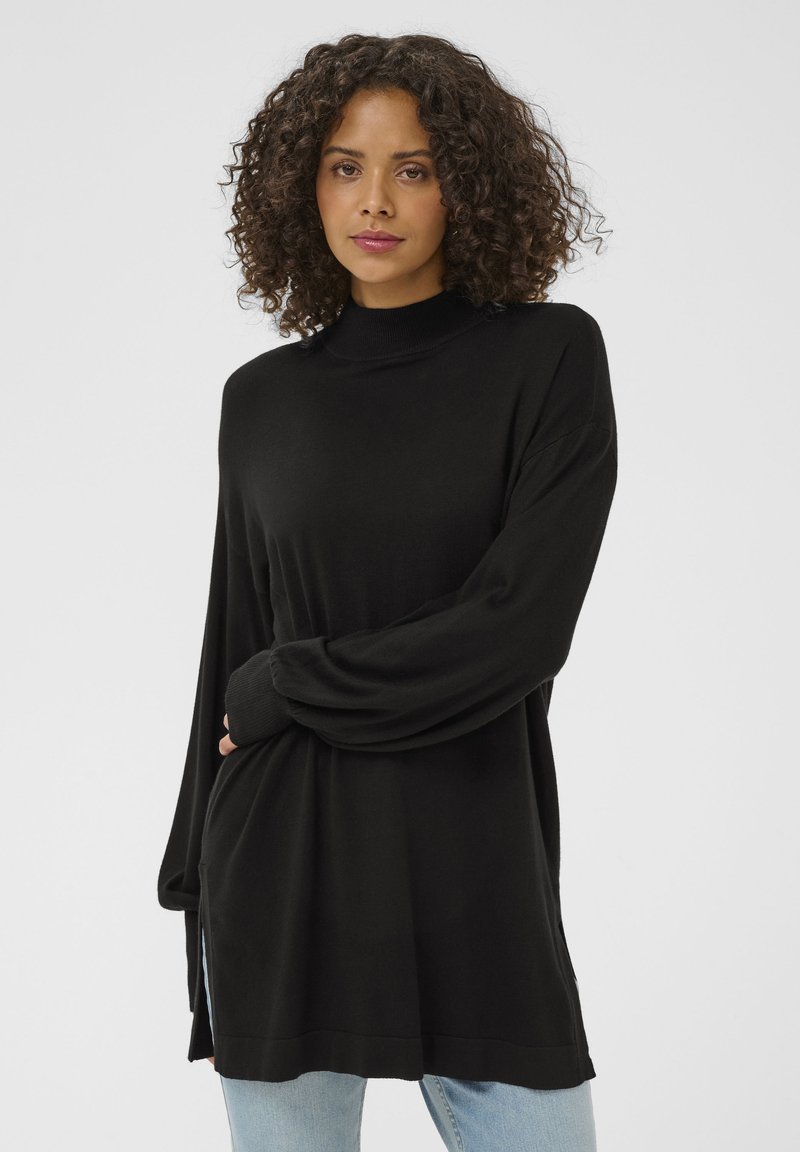 Pulover negru cu mâneci lungi și guler înalt, realizat dintr-un material moale și neted. Are o croială lejeră și crăpături laterale la tiv. Purta peste blugi deschis la culoare.