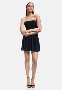 Zwart strapless jurk met geraffineerde lijfje en geplooide rok, gemaakt van lichtgewicht stof. Bevat een golvende zoom en wordt gedragen met zwarte hakken.