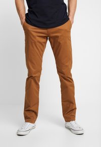 Men's brown cotton chino pants with a straight leg design,  pockets, and a smooth texture, paired with white sneakers.