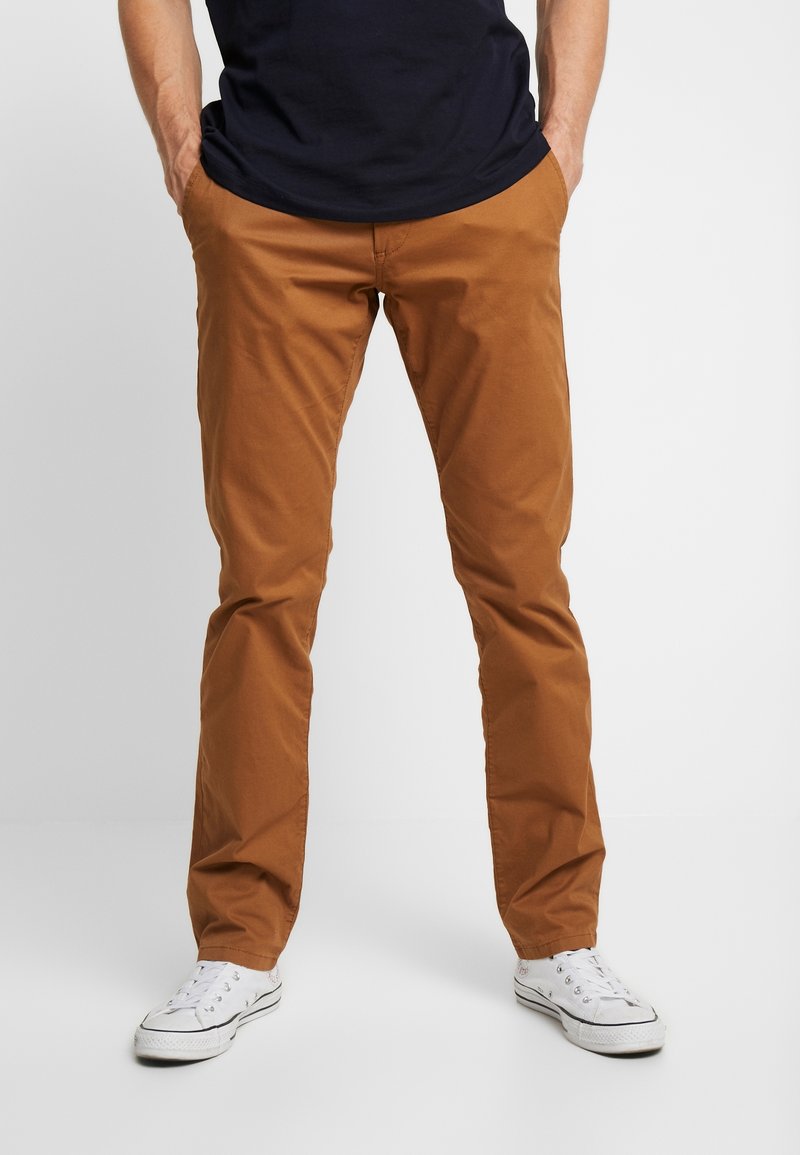 Men's brown cotton chino pants with a straight leg design,  pockets, and a smooth texture, paired with white sneakers.