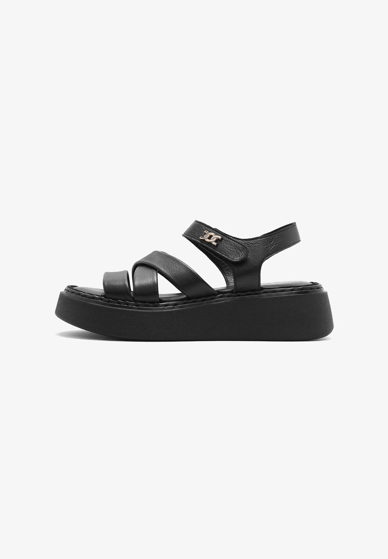 Black leather platform sandals featuring multiple cross-strap designs, adjustable heel strap, and a smooth textured sole. Silver logo accent.
