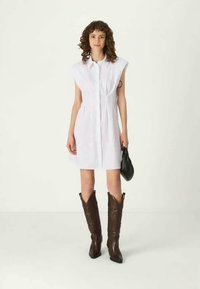 Λευκό φόρεμα με κοντά μανίκια, μπουτόν, λεπτομέρεια στη μέση, συνδυασμένο με καφέ καουμπόικες μπότες και μαύρη τσάντα.