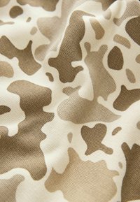 Beige tyg med ett brunt och vitt kamouflage-mönster, med en mjuk textur och en slät, stretchig väv för komfort.
