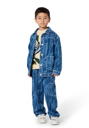 Jeansjacke und Hose in Blau mit Blattmuster. Die Jacke hat einen Kragen und Knopfverschluss; die Hose verfügt über eine Seitentasche. Weiße Turnschuhe.