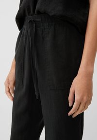 Svarta joggers med elastisk midja och snörning, med två sidofickor, avslappnad passform och en texturerad tygfinish.