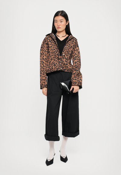 Leopardi mustriga jakk, millel on lai krae, nupulehe sulgemine ja kellukesed varrukad, koos mustade laia säärega pükstega ja terava nina kingadega.