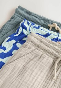 Trois paires de pantalons à coupe décontractée empilés. Couleurs : gris, beige et bleu avec un motif abstrait léger. Tissu doux et texturé, ceintures élastiques.