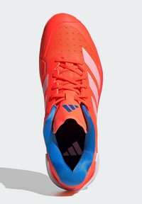 Red athletic shoe with a textured mesh upper, contrasting blue collar, and white stripes. Features a padded tongue and textured rubber sole.