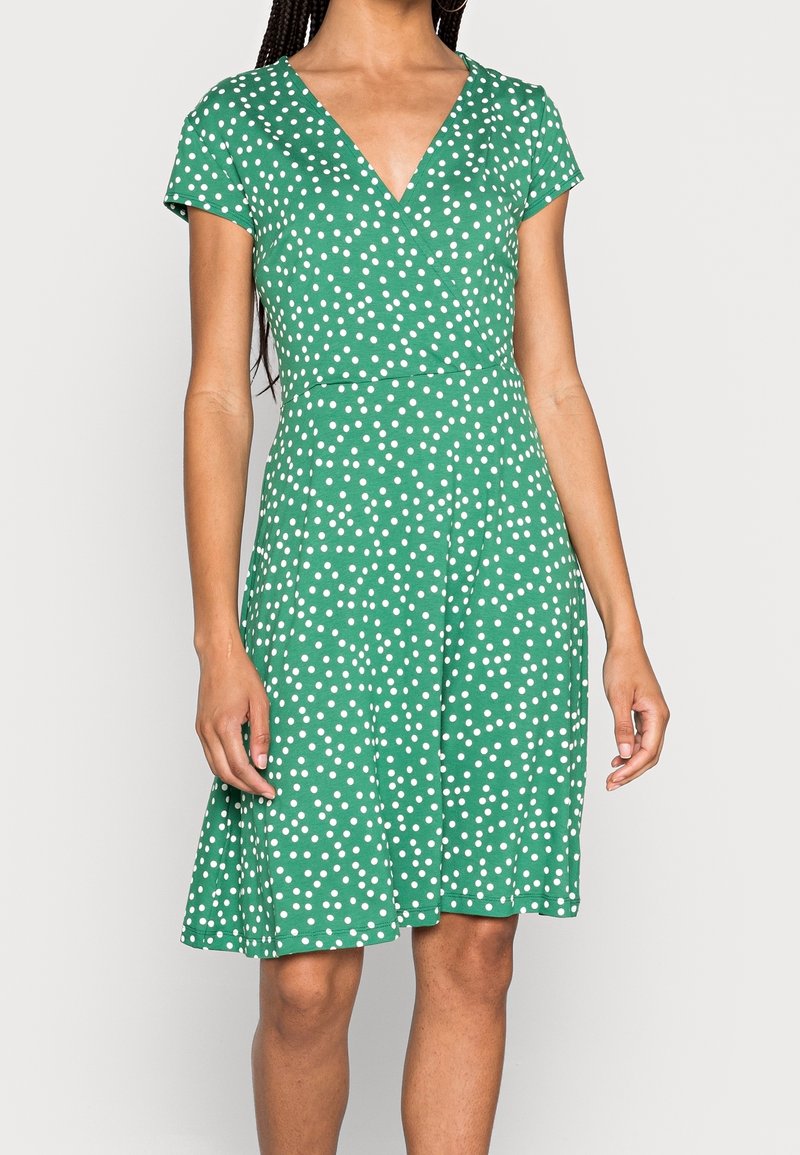 Zielona sukienka z krótkim rękawem i dekoltem w kształcie litery V, zdobiona białym wzorem w kropki, z dopasowaną talią i rozkloszowanym dołem. Wykonana z lekkiego materiału.