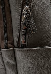 Borsa in pelle marrone dalla texture, con cerniera in metallo argentato. Presenta due cursori con incisioni del marchio. Vista ravvicinata dei dettagli della cerniera.