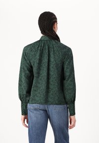 Blusa verde con motivo floreale realizzata in tessuto texturizzato, dotata di maniche lunghe, colletto alto e dettagli arricciati sul retro.