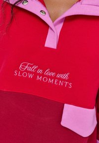 Czerwona i różowa koszula z kołnierzykiem z haftowanym napisem "Zakochaj się w WOLNYCH MOMENTACH" na piersi.
