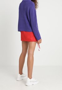 Fialový pletený svetr s krátkým střihem, zkombinovaný s červenou mini sukni. Oblečení doplňují bílé sportovní tenisky.