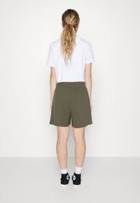T-shirt blanc, shorts côtelés verts olive, taille élastique, longueur genoux, associés à des baskets noires et des chaussettes blanches, vus de l'arrière.