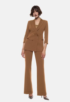 Blazer doppiopetto marrone su misura con pantaloni a zampa coordinati, entrambi in un tessuto liscio; presenta due tasche laterali e una leggera lucentezza.