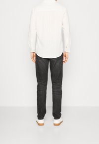 Chemise blanche à manches longues côtelée, assortie à un jean slim foncé et des baskets blanches. Design simple avec poignets boutonnés et ourlet droit.
